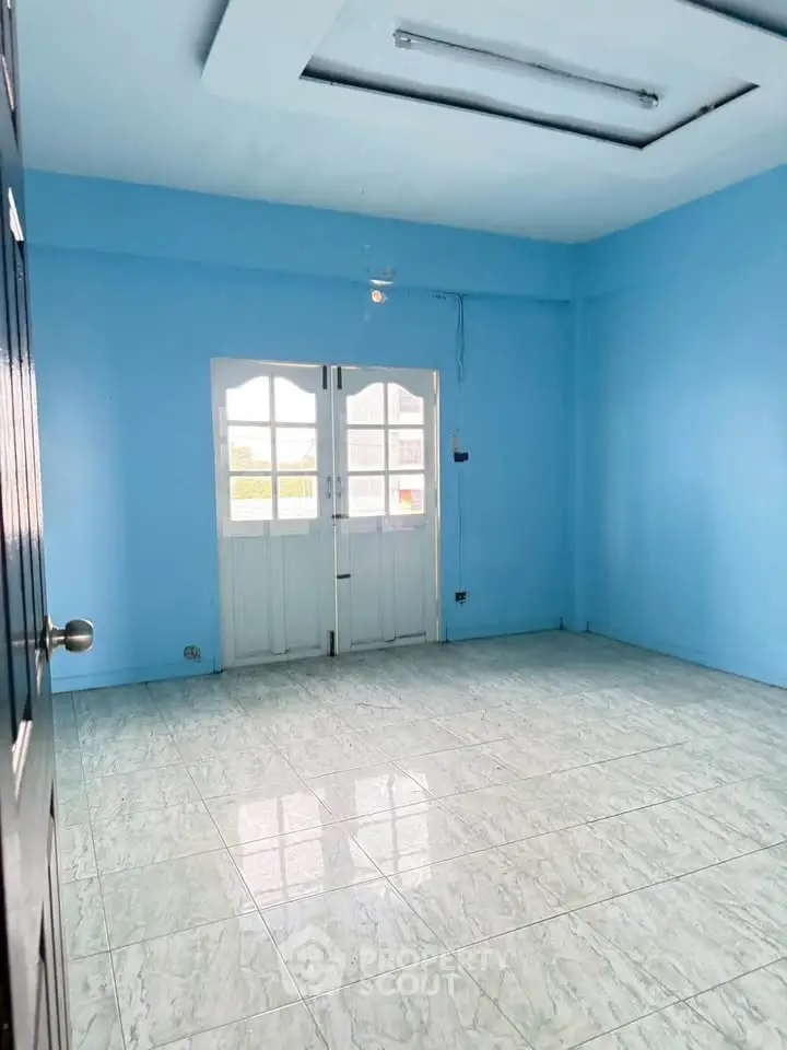 Spacious empty room with blue walls and tiled floor, featuring large windows for natural light.