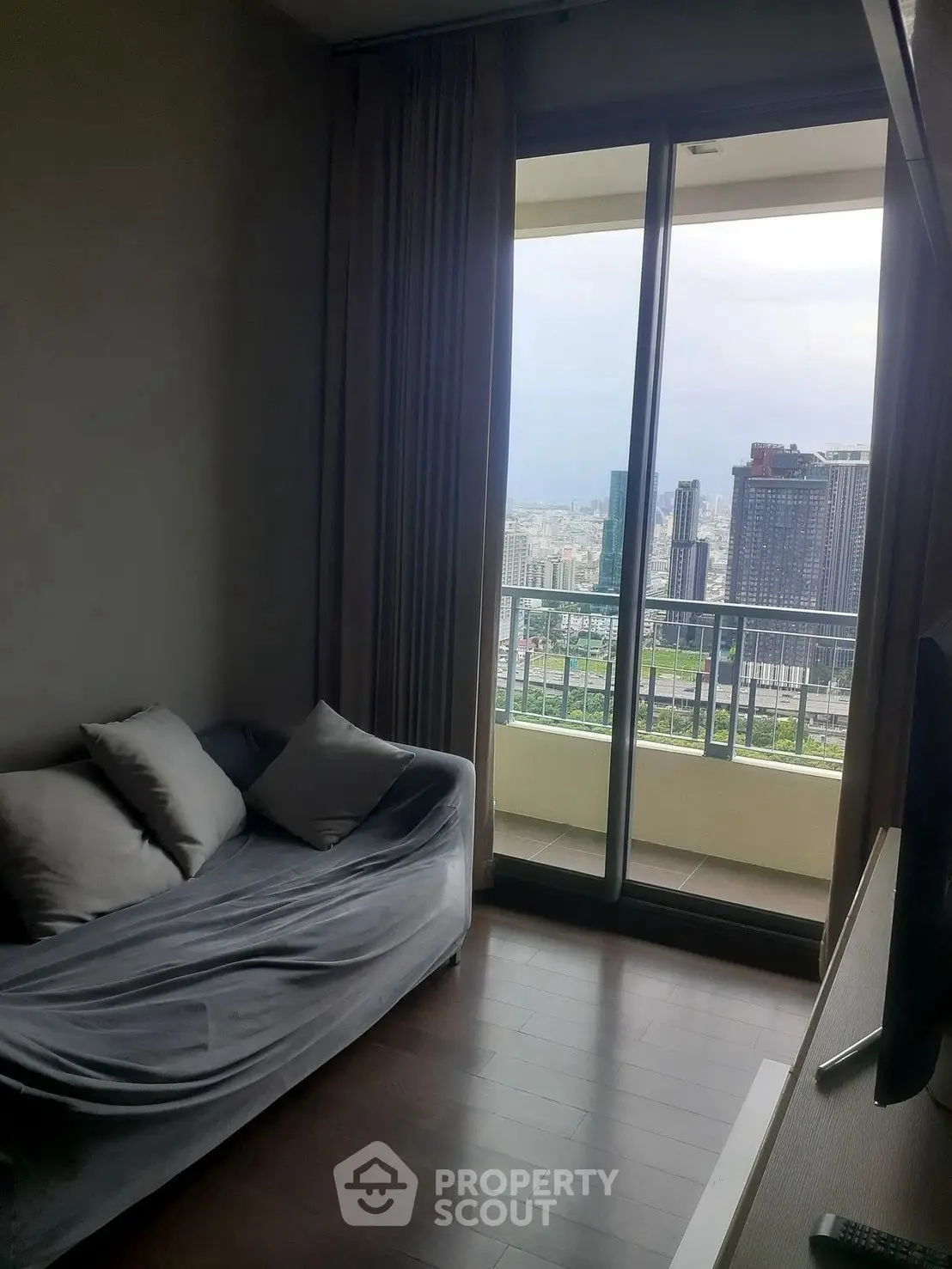Cozy living room with city view from balcony, featuring a comfortable sofa and floor-to-ceiling windows.