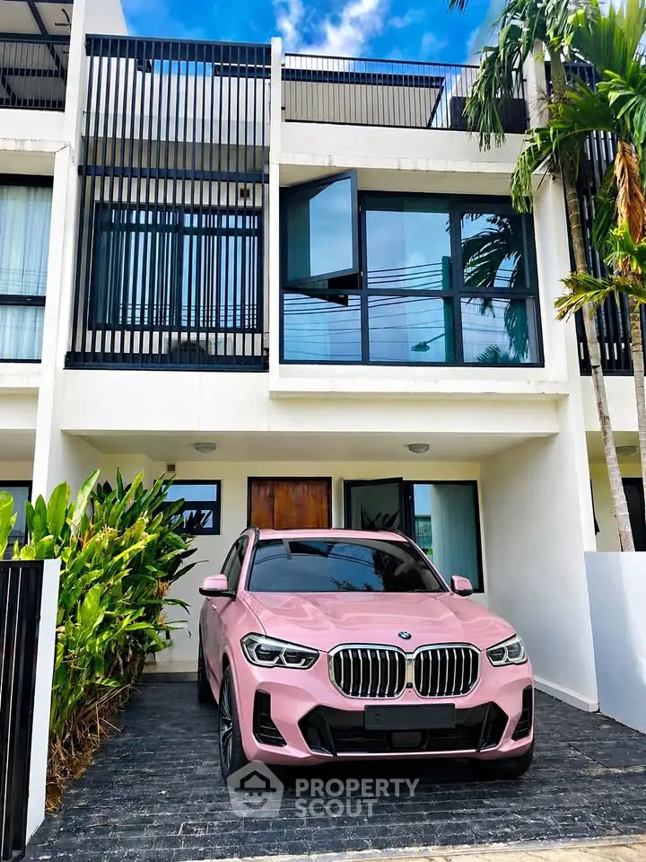 Modern townhouse with sleek facade and luxury car parked in driveway, surrounded by lush greenery.