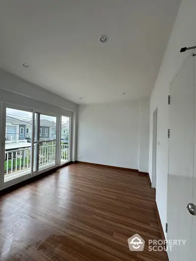 Spacious room with wooden flooring and large windows overlooking a serene neighborhood.