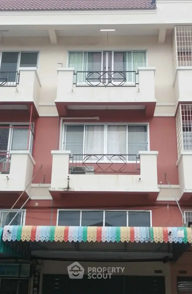 Charming multi-story residential building with colorful awning and balconies in urban setting.