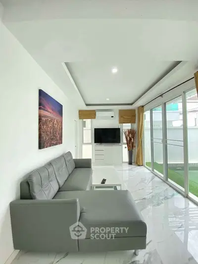 Modern living room with sleek gray sofa, large windows, and stylish decor in a bright, open space.