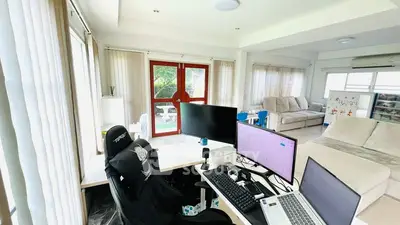 Spacious living room with modern home office setup and large windows for natural light.