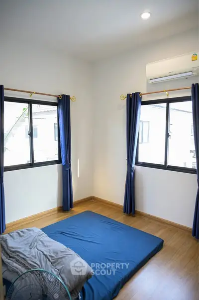 Minimalist bedroom with wooden flooring and blue curtains