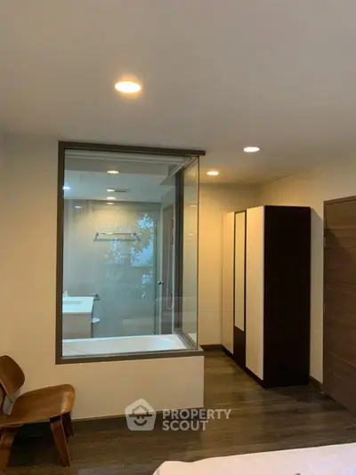 Modern bedroom with glass wall view into luxurious bathroom featuring a sleek bathtub.