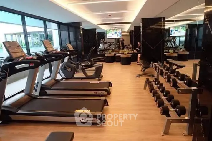 Luxurious gym with modern equipment and floor-to-ceiling windows in upscale residential building.