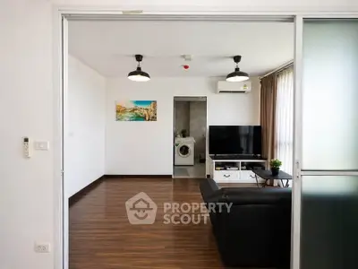 Spacious modern living room with sleek wooden flooring and stylish lighting, featuring a cozy black sofa and a flat-screen TV.