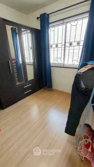 Cozy bedroom with wooden floor, wardrobe, and window with bars.