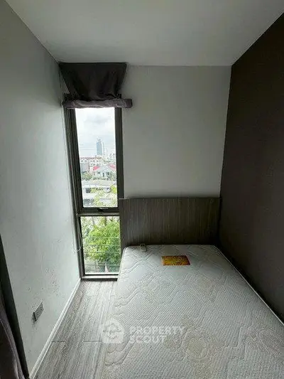 Cozy bedroom with large window offering city view, perfect for urban living.