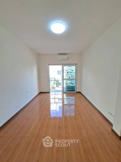Spacious empty room with glossy wooden floors and large window for natural light.