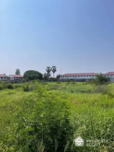 Expansive undeveloped land offering a blank canvas for building, set against a backdrop of residential buildings under a clear blue sky.