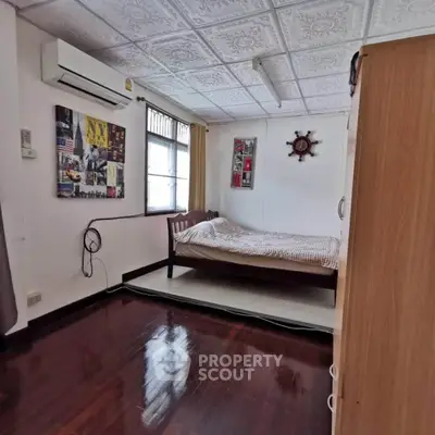 Cozy bedroom with wooden flooring and decorative ceiling tiles, featuring a bed and wall art.