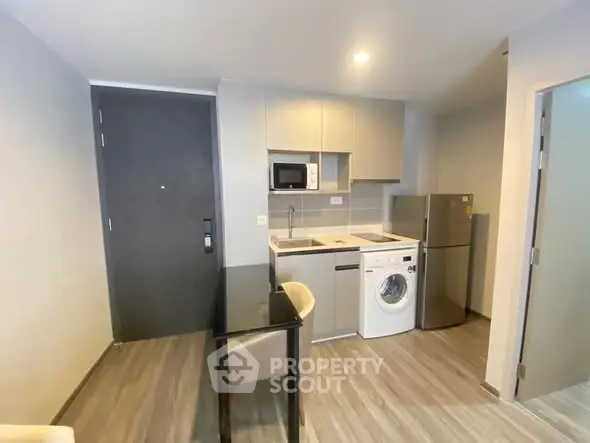 Modern compact kitchen with washing machine and fridge in sleek apartment.