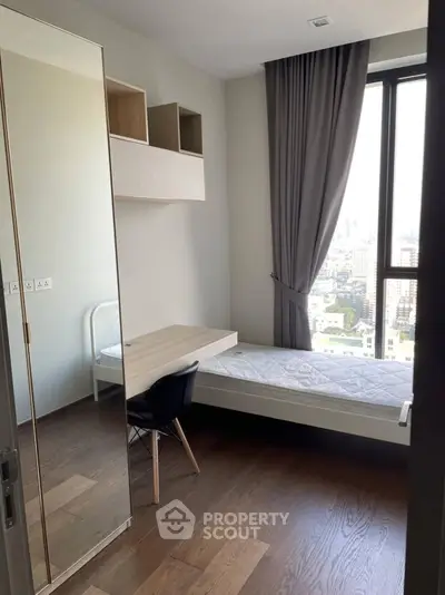 Modern bedroom with city view, featuring sleek furniture and large window for natural light.