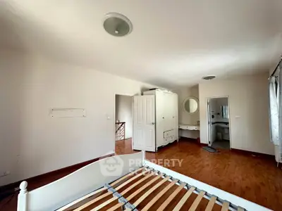 Spacious bedroom with wooden flooring and white furniture, featuring a bed frame and wardrobe.