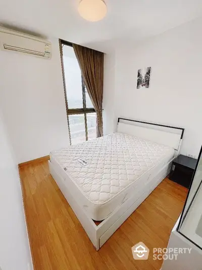 Bright and airy bedroom with large window offering natural light, complemented by wooden flooring and minimalist decor, perfect for restful living.