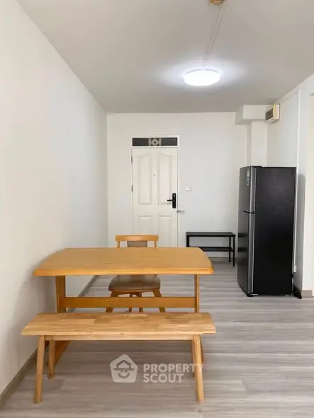 Minimalist dining area with wooden table and chairs, modern fridge, and sleek flooring.