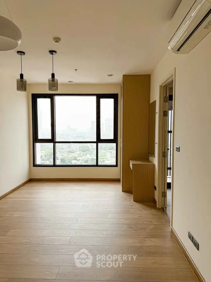 Spacious empty room with large window offering city view and wooden flooring.