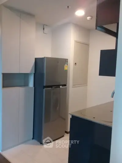 Modern kitchen with sleek cabinets and stainless steel fridge in compact layout.