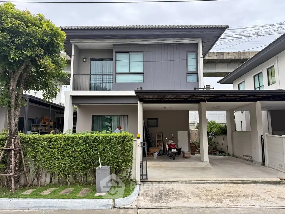Modern two-story house with carport and lush greenery in suburban neighborhood.