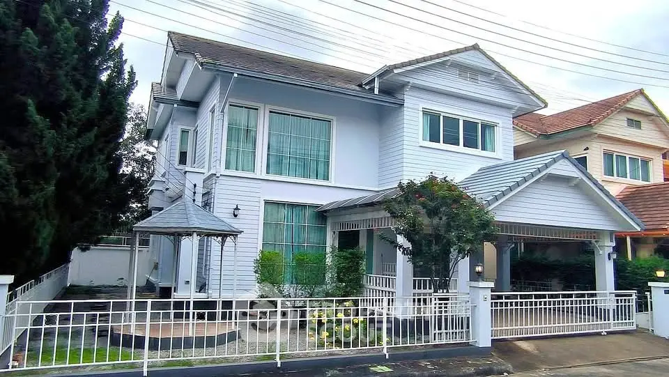 Charming two-story house with a white picket fence and lush greenery, perfect for family living.