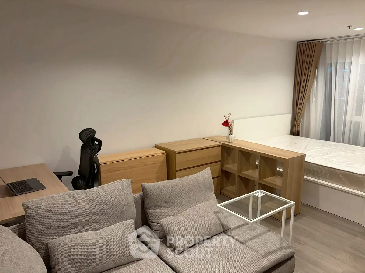 Modern studio apartment with cozy living area and workspace, featuring neutral tones and natural light.