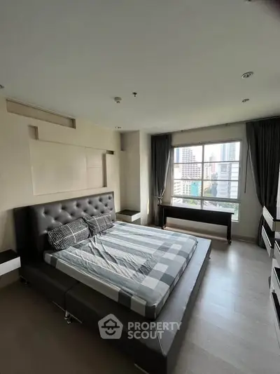 Spacious bedroom with modern decor and city view, featuring a large bed and ample natural light.