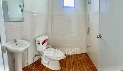 Modern bathroom with white tiles and wooden floor, featuring a shower and toilet.