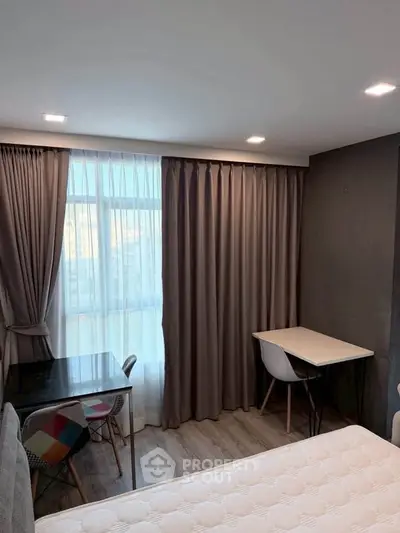 Cozy bedroom with modern decor and natural light, featuring a study area and elegant curtains.