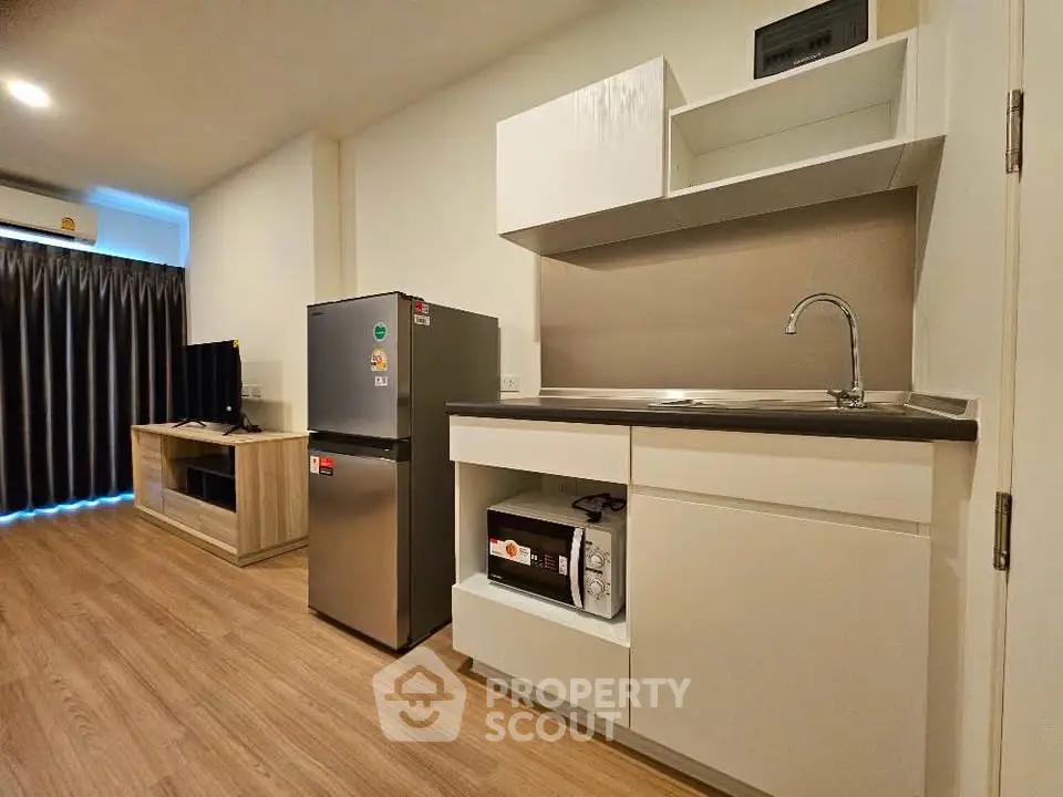 Modern studio apartment with sleek kitchen and cozy living area, featuring wood flooring and contemporary appliances.
