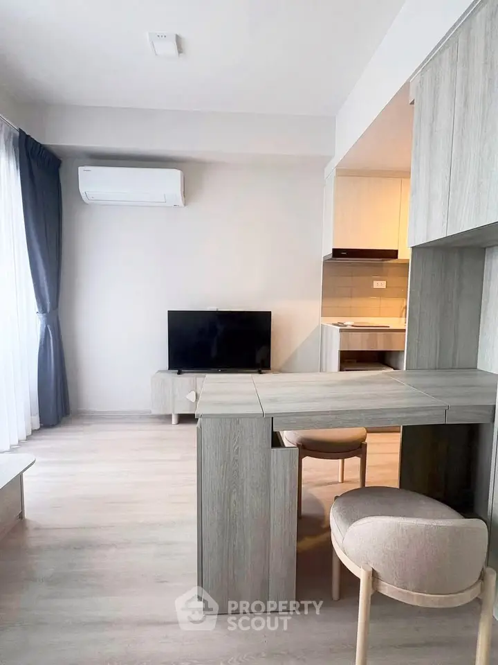 Modern living room with sleek furniture and open kitchen layout, featuring a cozy dining area and natural light.