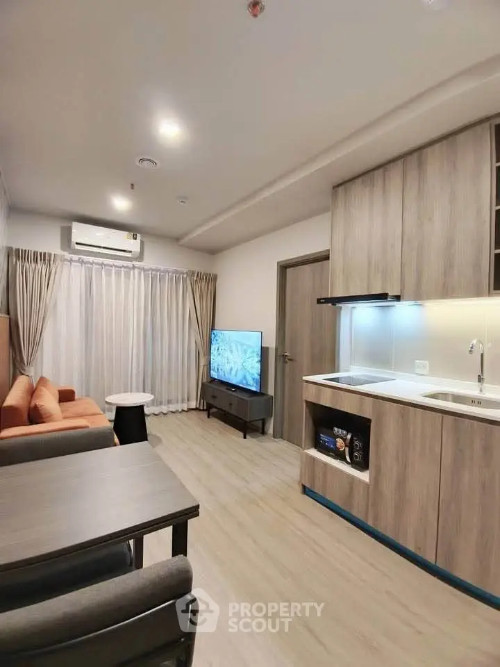 Modern living room with integrated kitchen, featuring sleek cabinetry and cozy seating area.