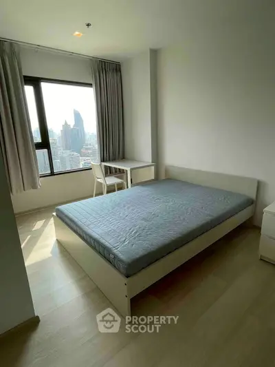 Bright bedroom with city view, featuring a bed and study desk, ideal for urban living.