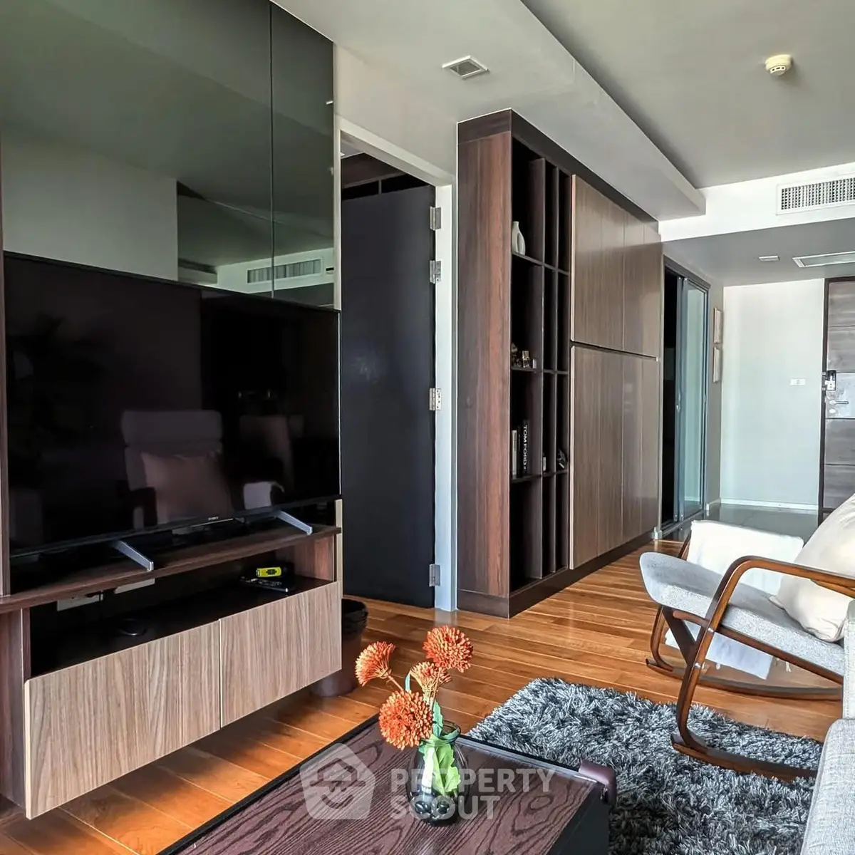 Modern living room with sleek furniture and wooden flooring, featuring a large TV and stylish decor.