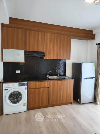 Modern kitchen with wooden cabinets, washing machine, and fridge in a sleek apartment.