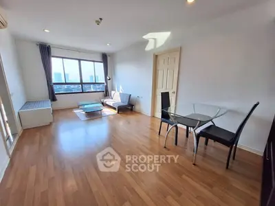 Spacious living room with wooden flooring and city view, featuring modern furniture and large windows.