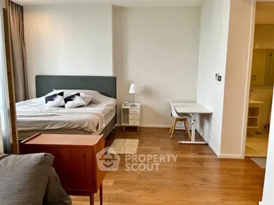 Modern bedroom with cozy bed, wooden flooring, and study desk in a stylish apartment.
