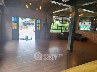 Spacious industrial-style living room with large windows and brick walls.
