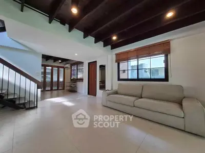 Spacious living room with modern design and natural light, featuring a cozy sofa and wooden ceiling beams.