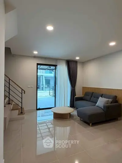 Modern living room with sleek design, featuring a cozy sectional sofa and large glass door leading to outdoor space.