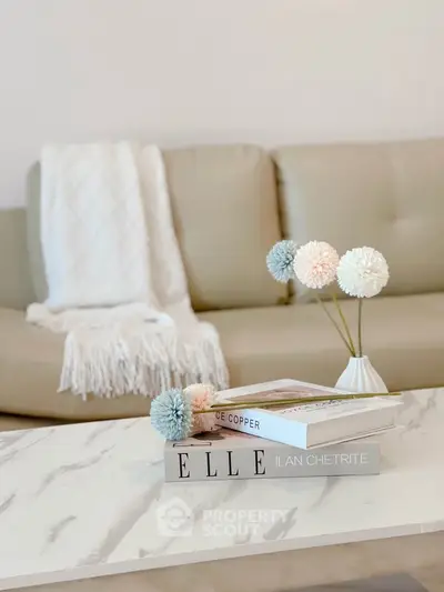 Stylish living room with beige sofa, marble coffee table, and decorative books and flowers.