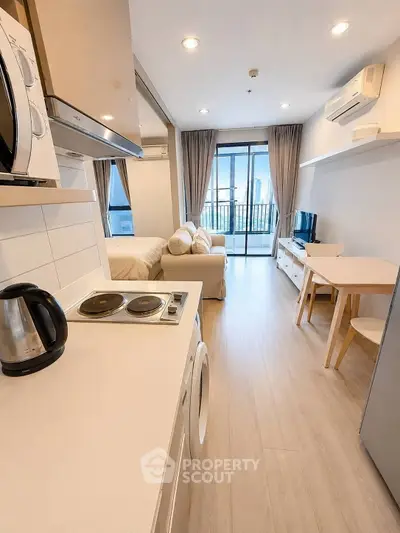 Modern open-plan studio apartment with balcony and city view, featuring compact kitchen and cozy living area.