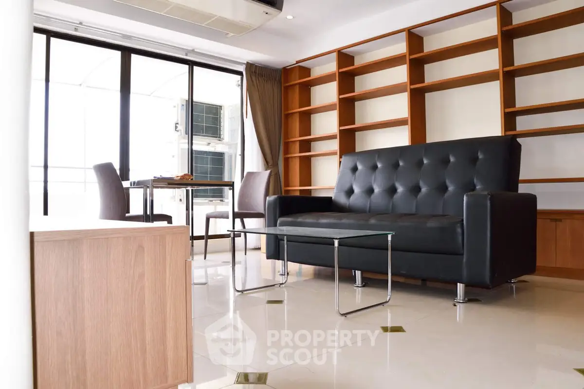 Modern living room with sleek black sofa, glass coffee table, and built-in wooden shelves.