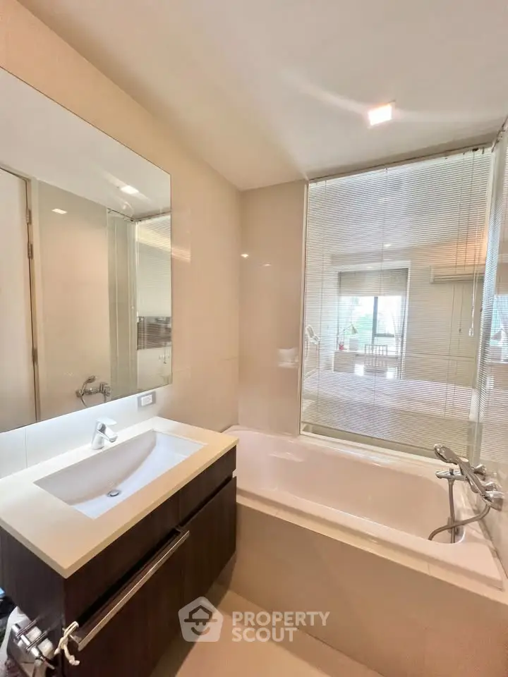 Modern bathroom with sleek fixtures and a bathtub, featuring a large mirror and natural light.