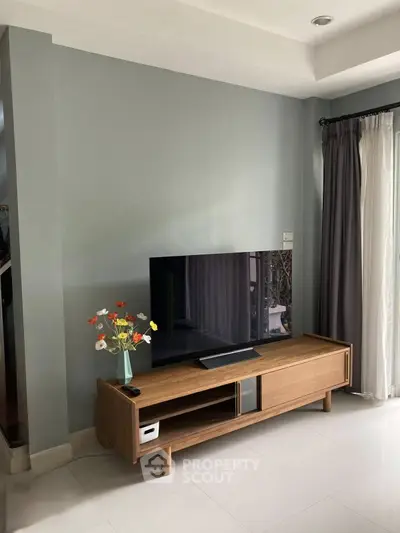 Modern living room with sleek TV stand and large flat-screen TV, complemented by elegant curtains and a vase of flowers.