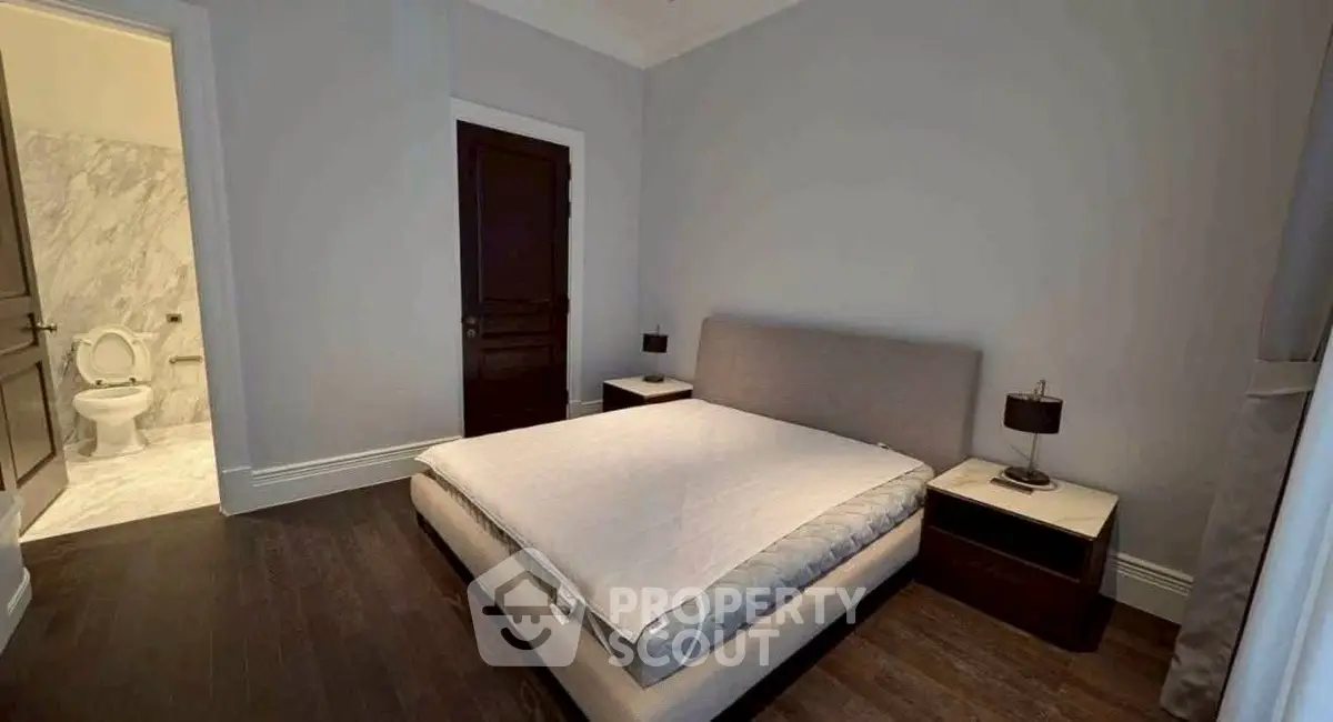 Modern bedroom with ensuite bathroom, featuring sleek dark wood flooring and contemporary furnishings.