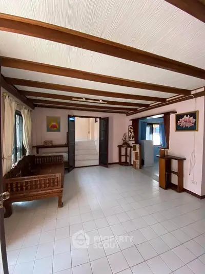 Charming living room with wooden beams and tiled floor, featuring traditional furniture and ample natural light.