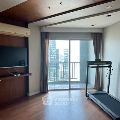 Modern apartment with treadmill and balcony view, featuring sleek wooden flooring and large TV.