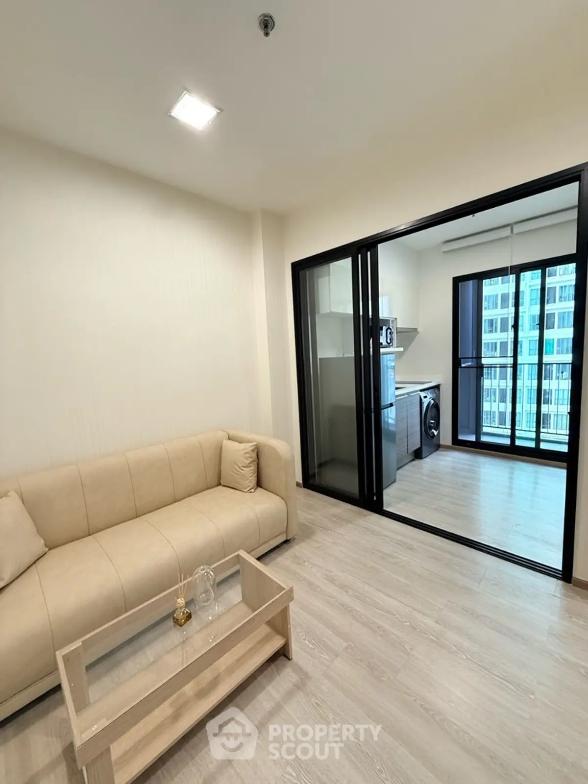 Modern living room with beige sofa and glass coffee table, adjacent to a sleek kitchen.