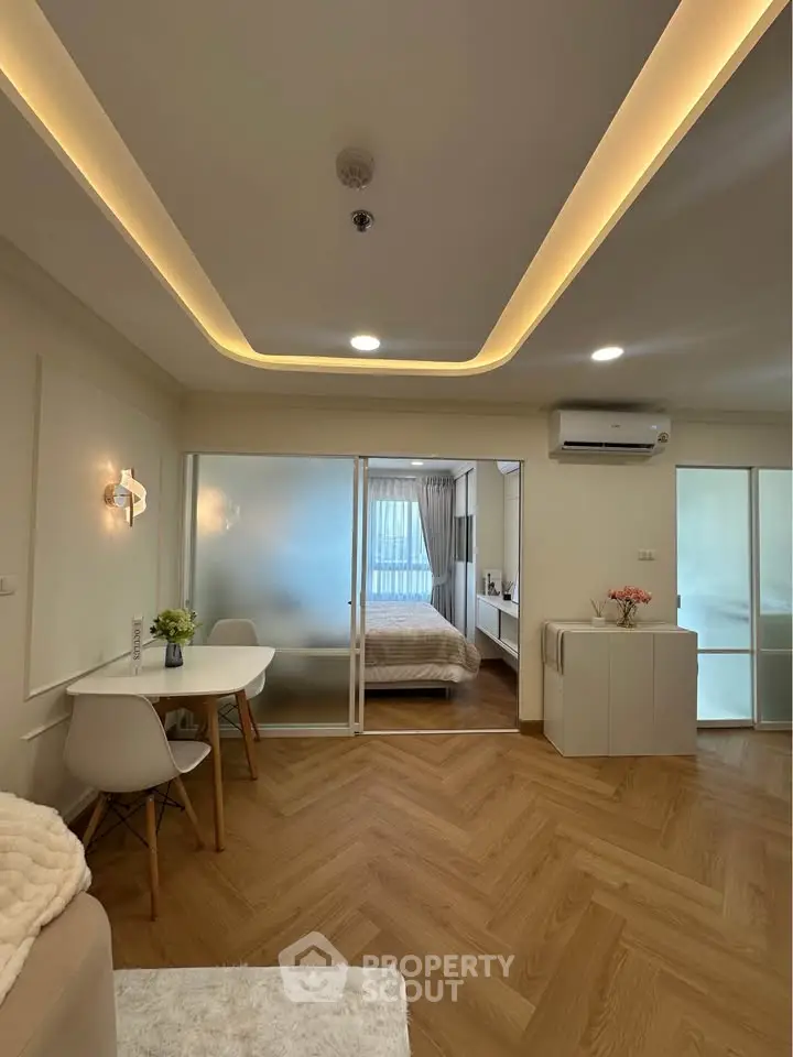 Modern living room with elegant lighting and cozy dining area, featuring a view into a stylish bedroom.